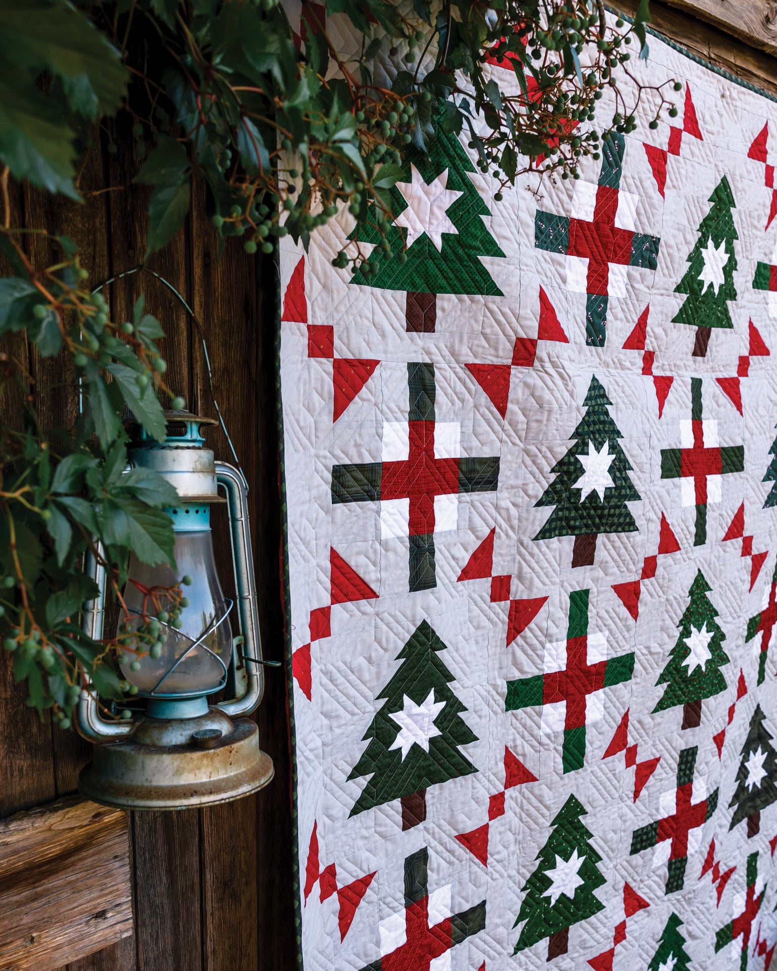 Hanging quilt with green pine trees and other red and green designs on a white base