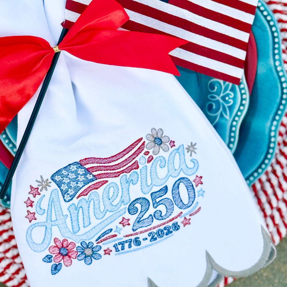 Embroidered towel with American flag design and 'America 250' text, placed on a decorative plate with a red and white checkered cloth.