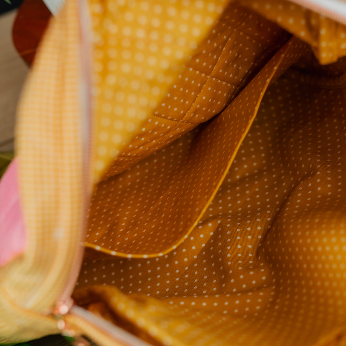 Close-up of the interior of a fabric zippered pouch or bag, showing a mustard yellow and white polka dot lining with a white zipper.