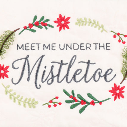 Embroidered holiday text reading 'MEET ME UNDER THE Mistletoe' in dark gray, surrounded by a wreath of red poinsettias, green pine needles, and light green leaves on a white fabric background.