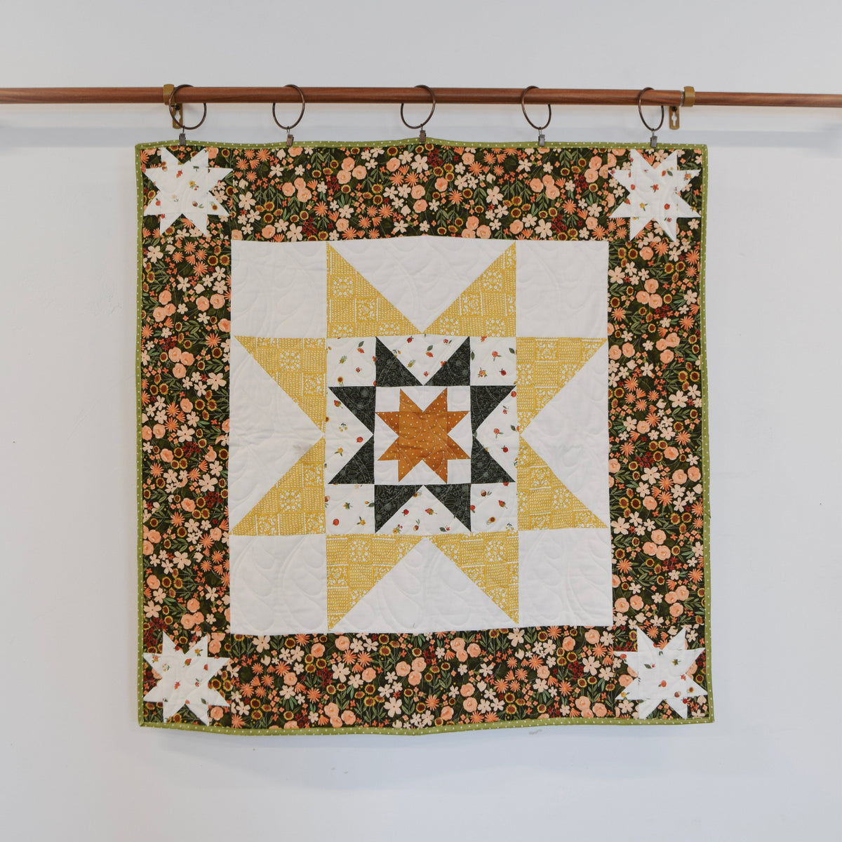 Quilt with star pattern hanging on a rack against a white background