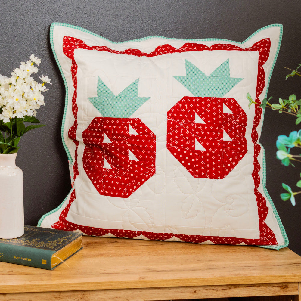 Decorative pillow with red and green patterns on a wooden surface with a dark background