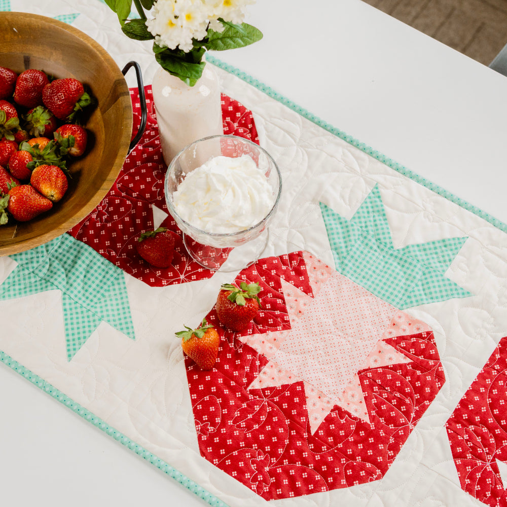 Table setting with strawberries, a bowl of strawberries, and a decorative tablecloth featuring star patterns.