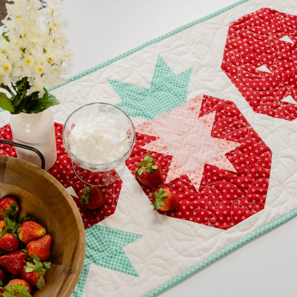 Quilted table runner with star pattern, strawberries, and a glass of milk on a table.