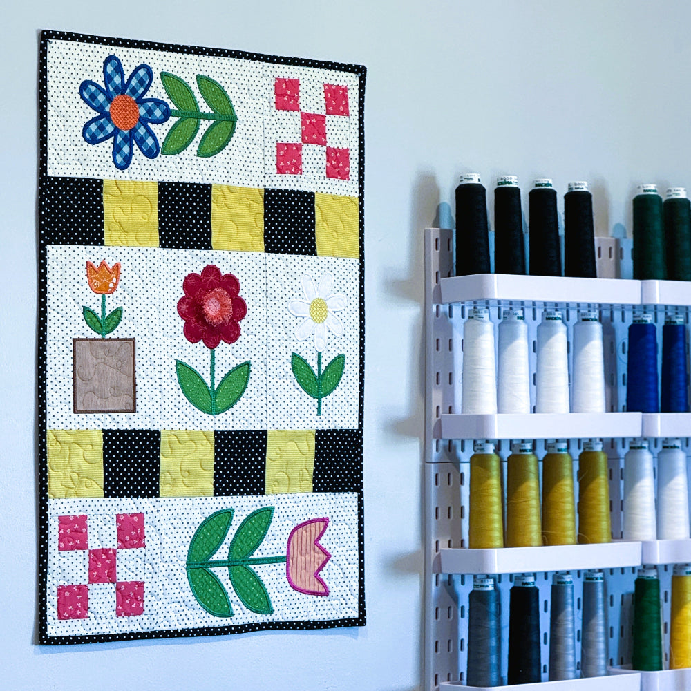 Colorful quilt with floral patterns hanging on a wall next to a thread rack.