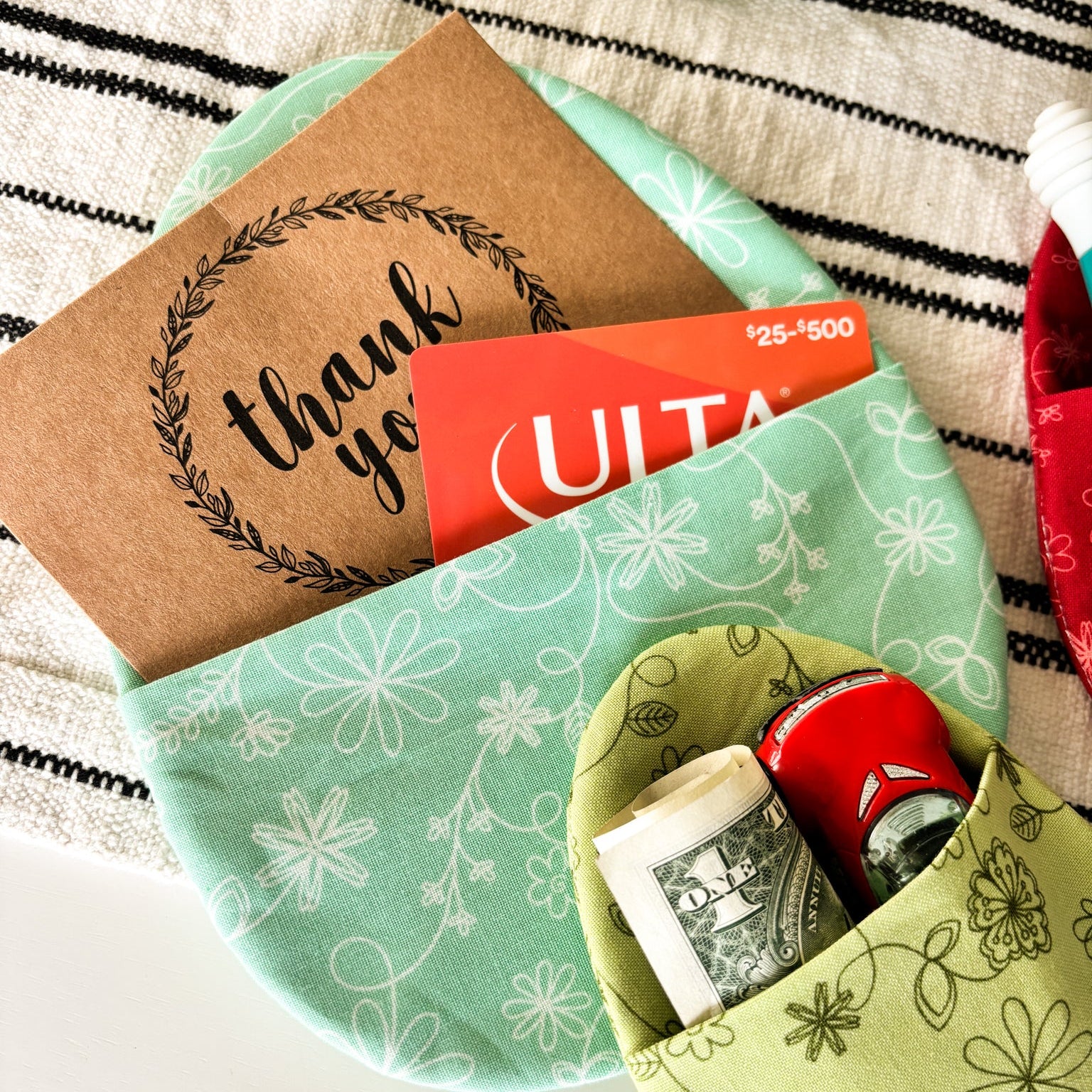 Green fabric pouch with money and a gift card on a striped surface