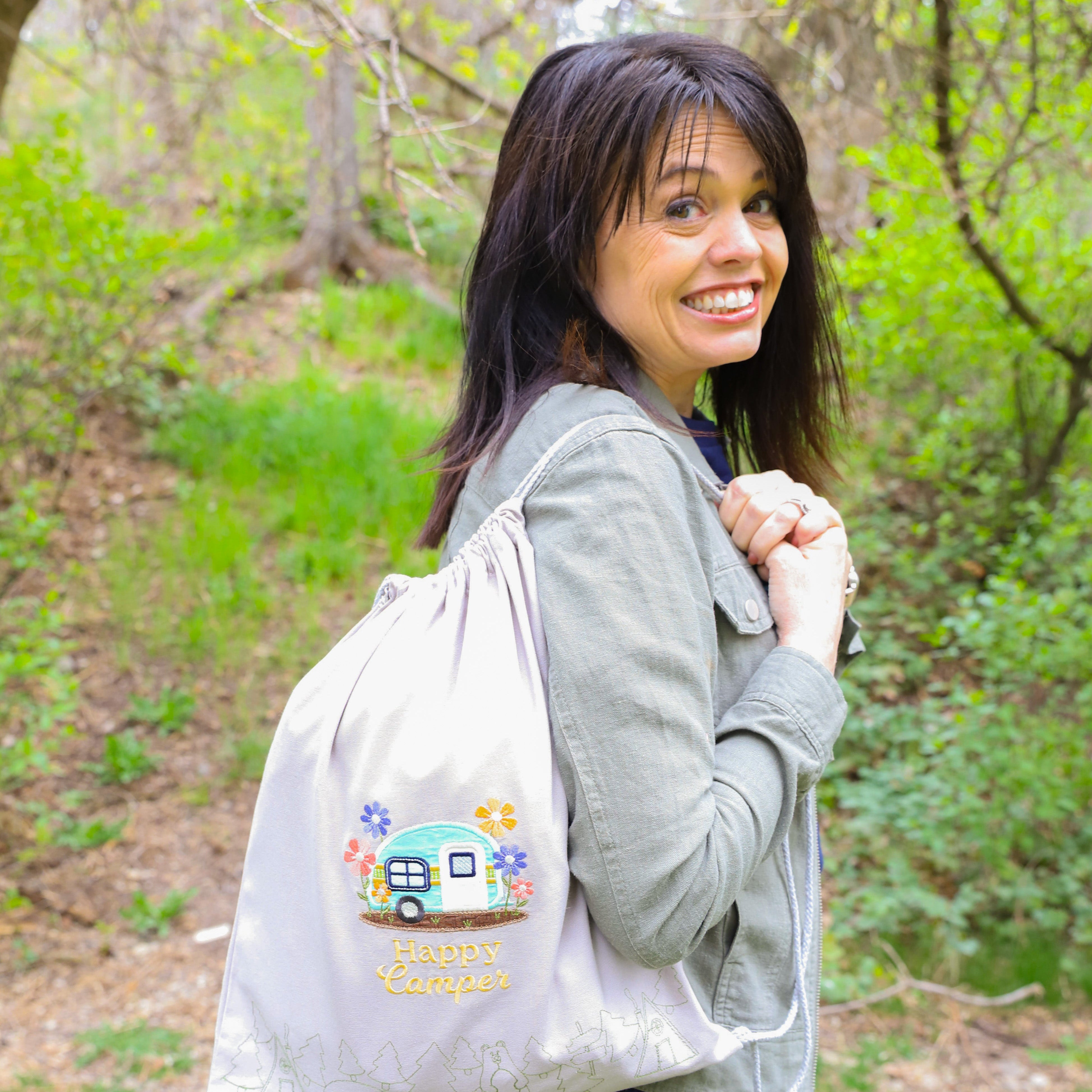 Woman holding a drawstring bag with colorful designs in a forest setting