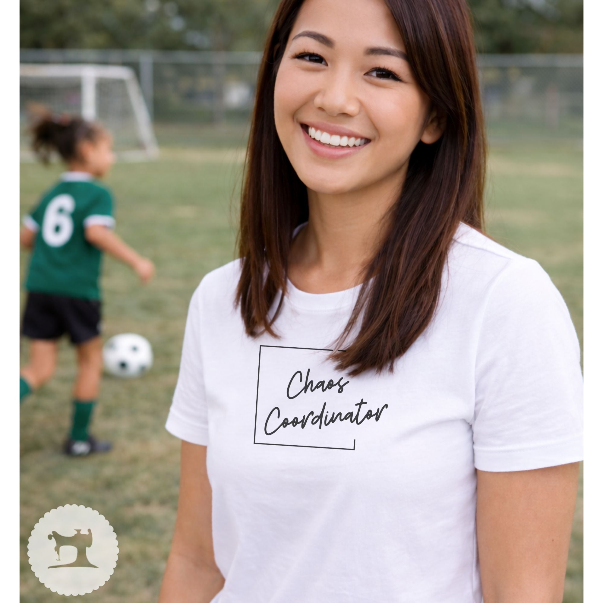 Woman wearing a white t-shirt with 'Chaos Coordinator' text on a soccer field.