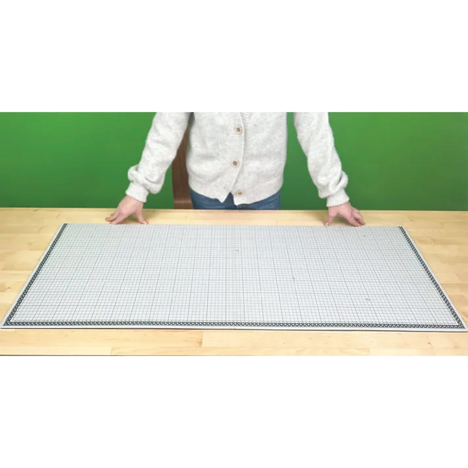 Person standing behind a large grid mat on a wooden surface with a green background