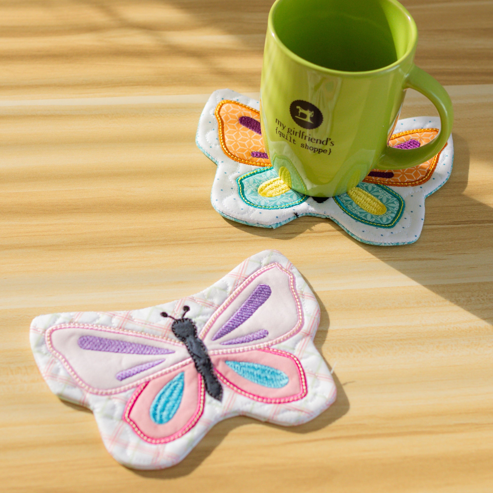 Butterfly-shaped coasters on a wooden surface with a green mug.