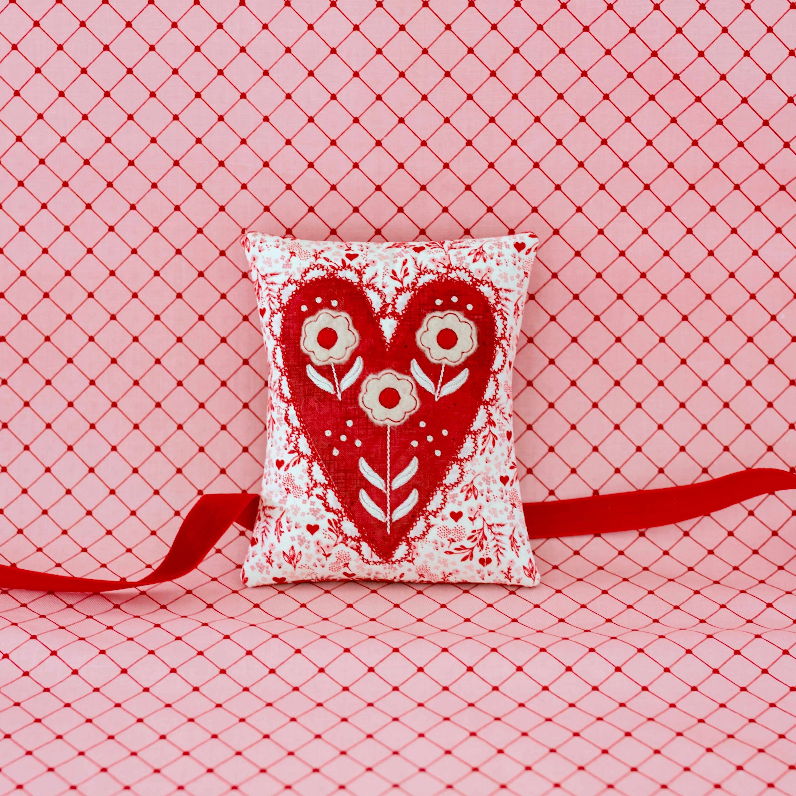 Decorative pillow with heart design and red ribbon on a pink grid background
