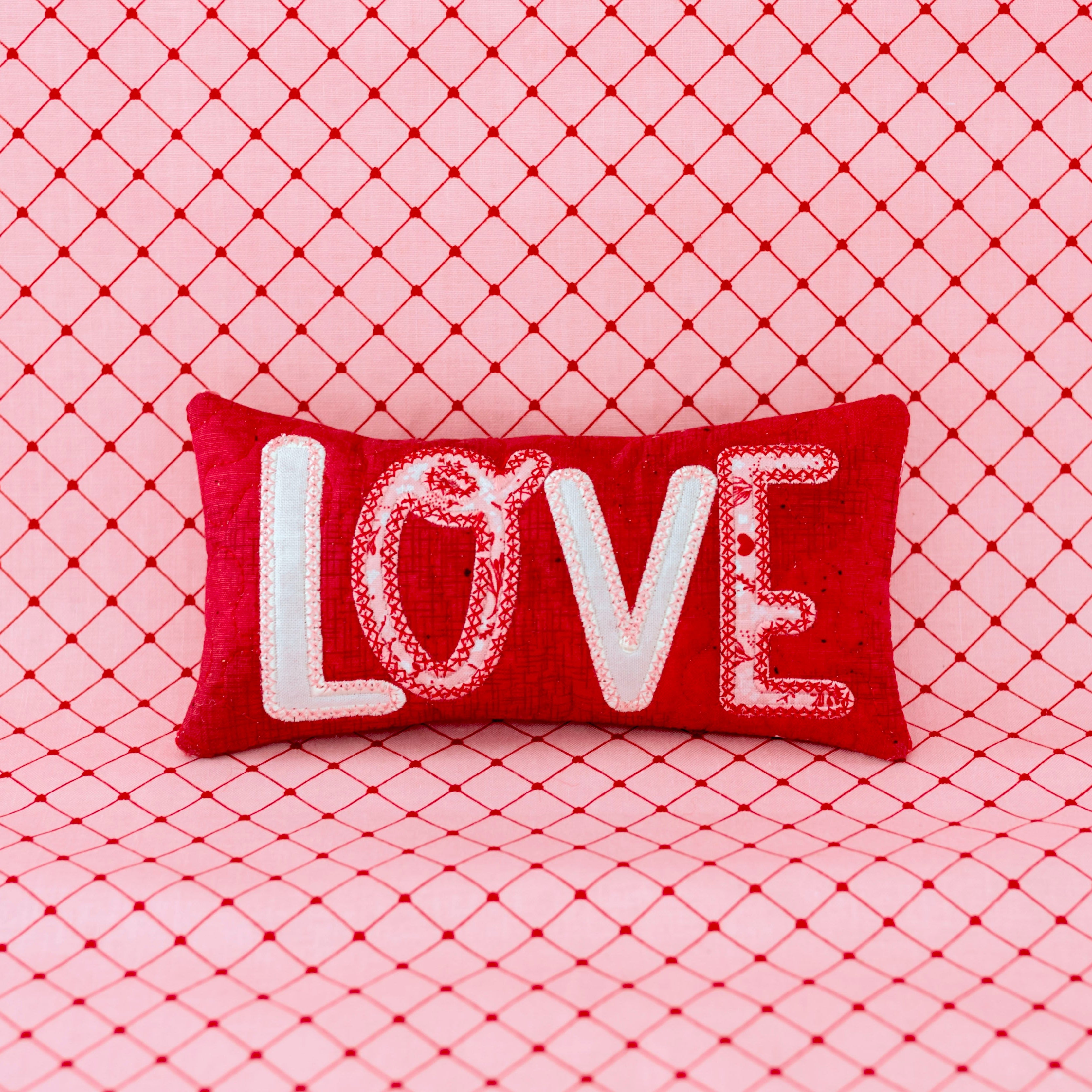 Red pillow with 'LOVE' text on a pink textured background