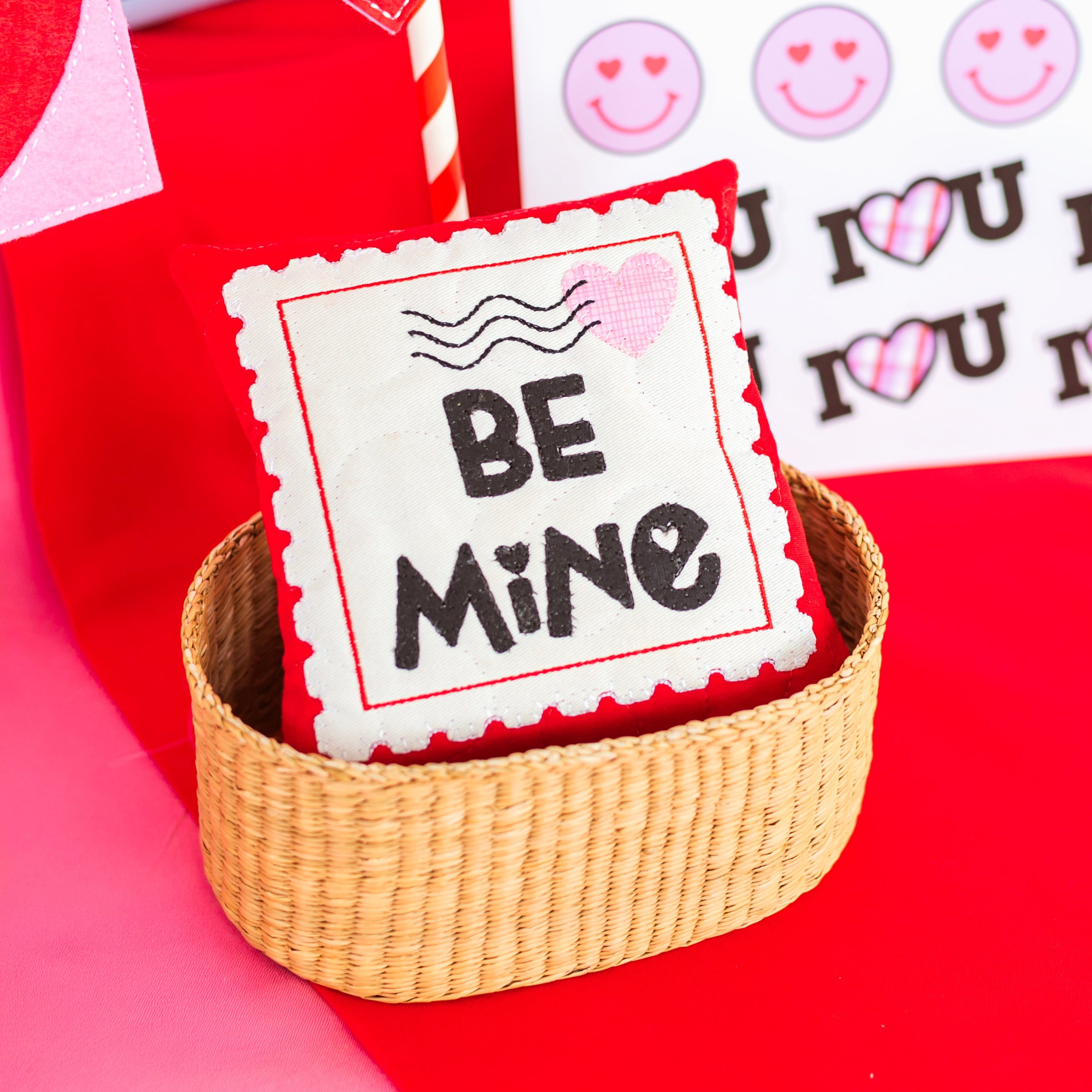 Valentine's Day-themed pillow with 'Be Mine' text in a basket on a red background.