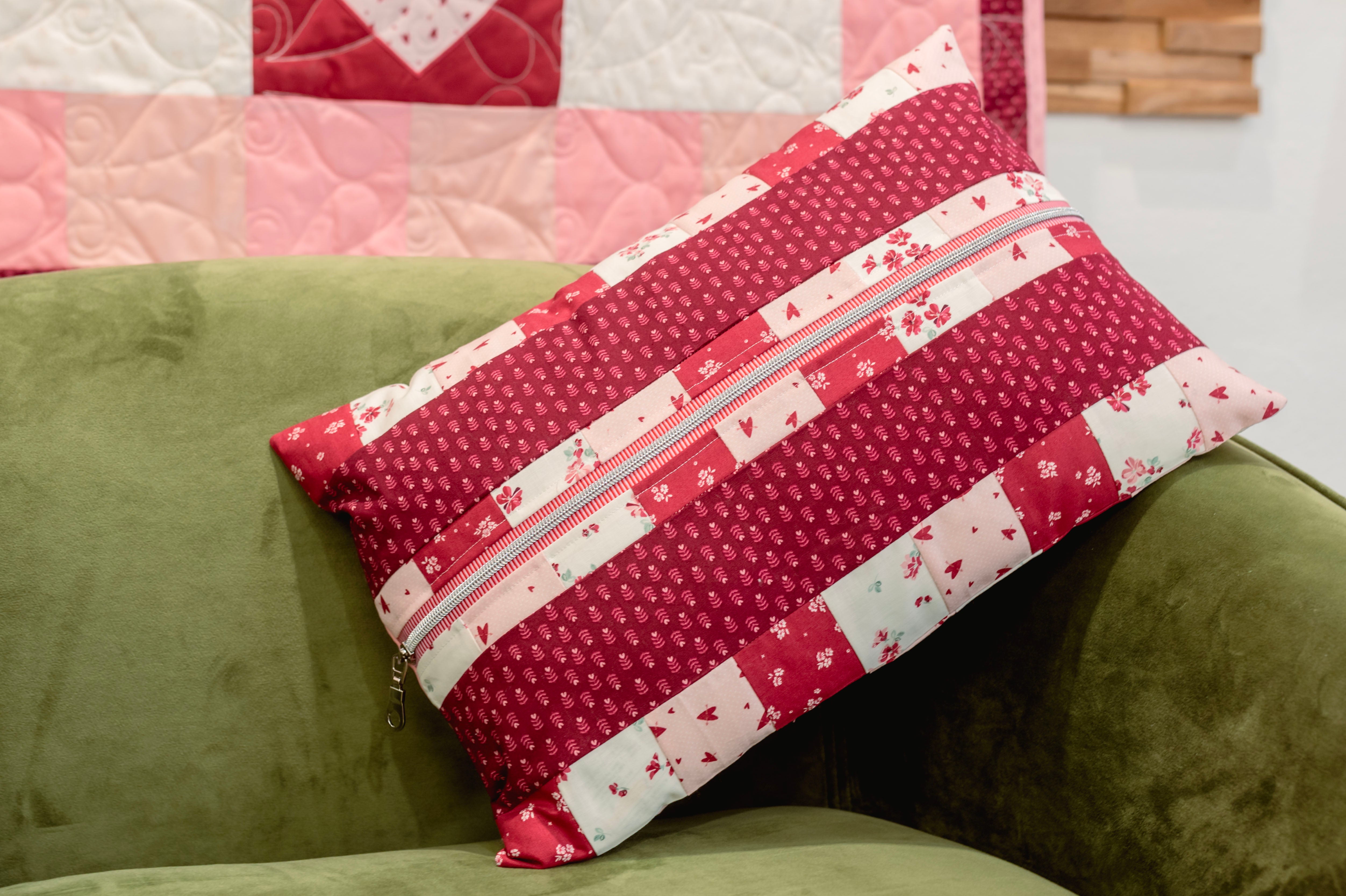 Red and white patterned pillow with a zipper on a green couch