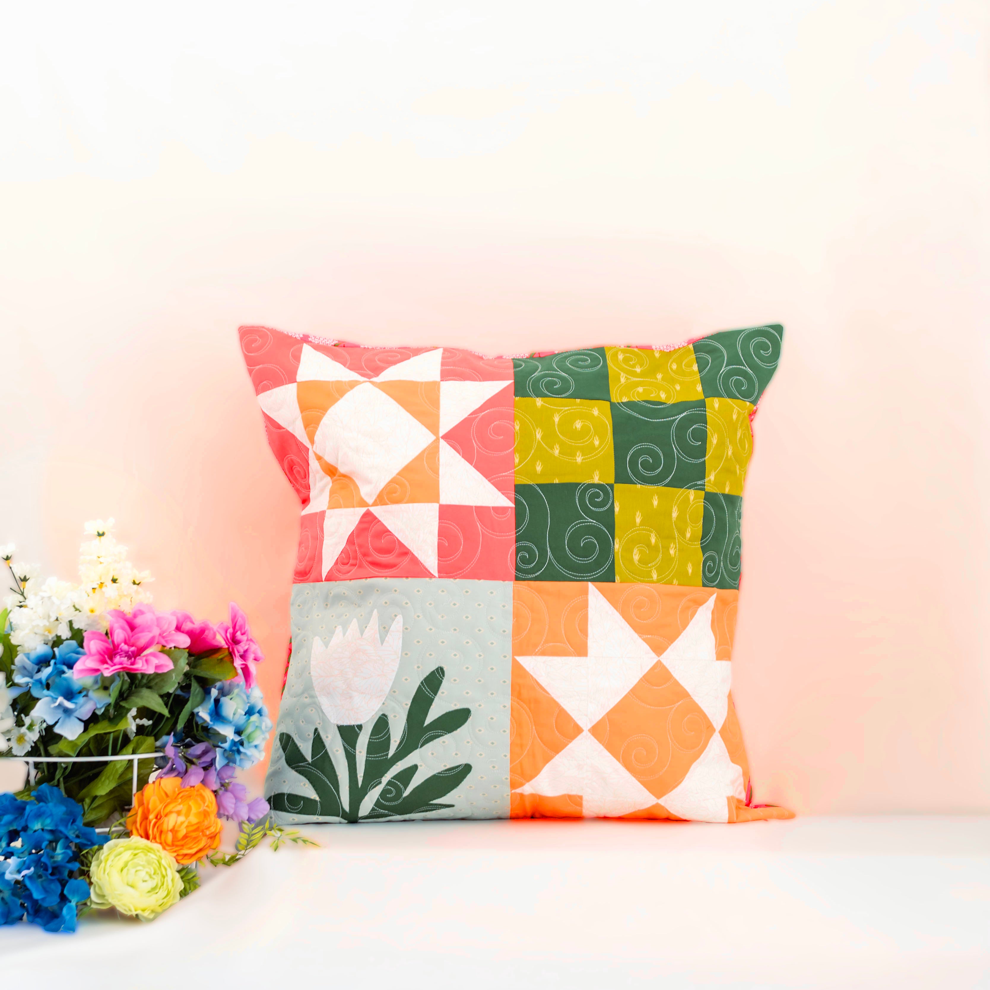 Colorful geometric-patterned pillow on a white surface with flowers in the background