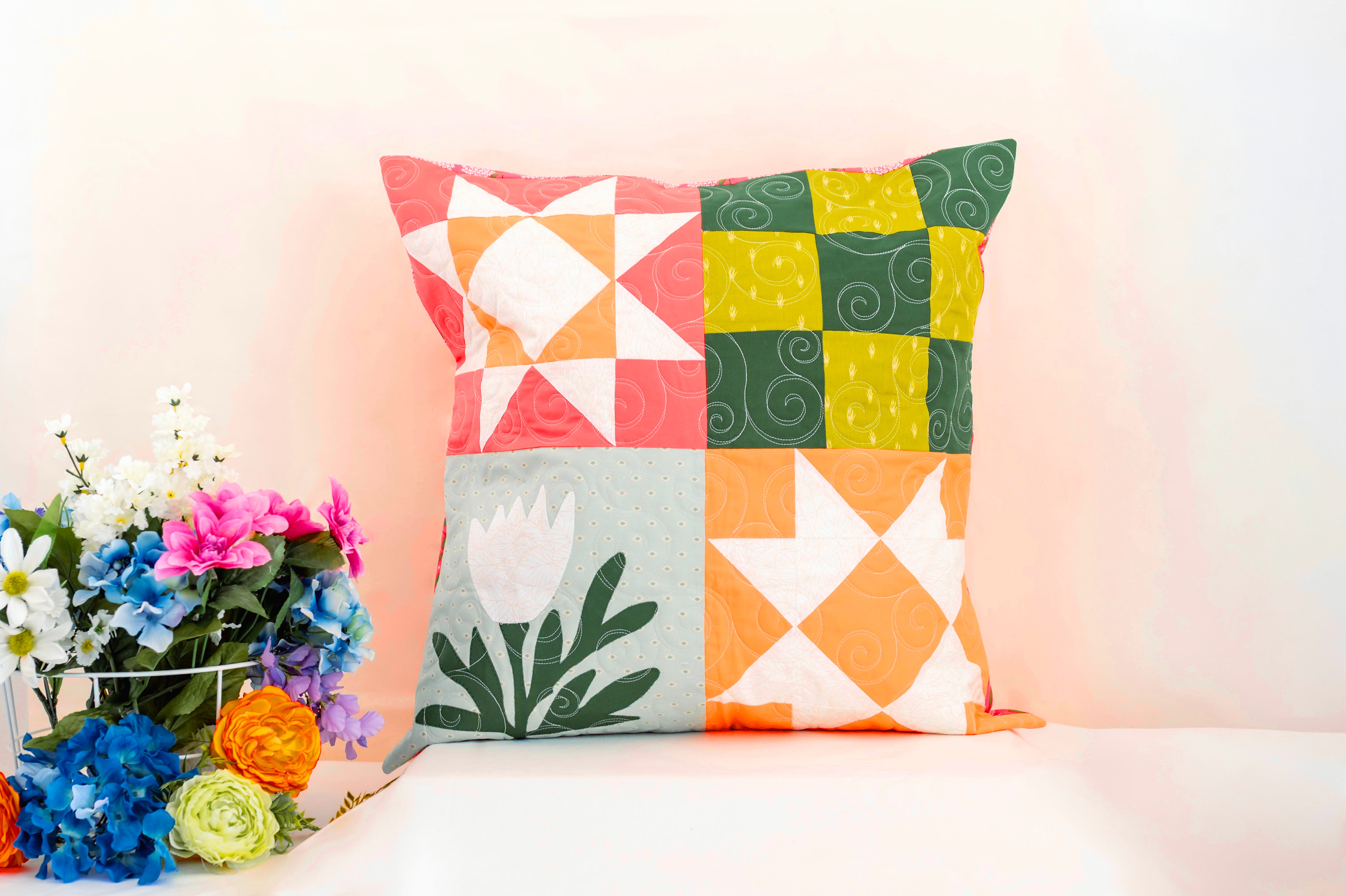 Colorful patchwork pillow on a white surface with flowers in the background