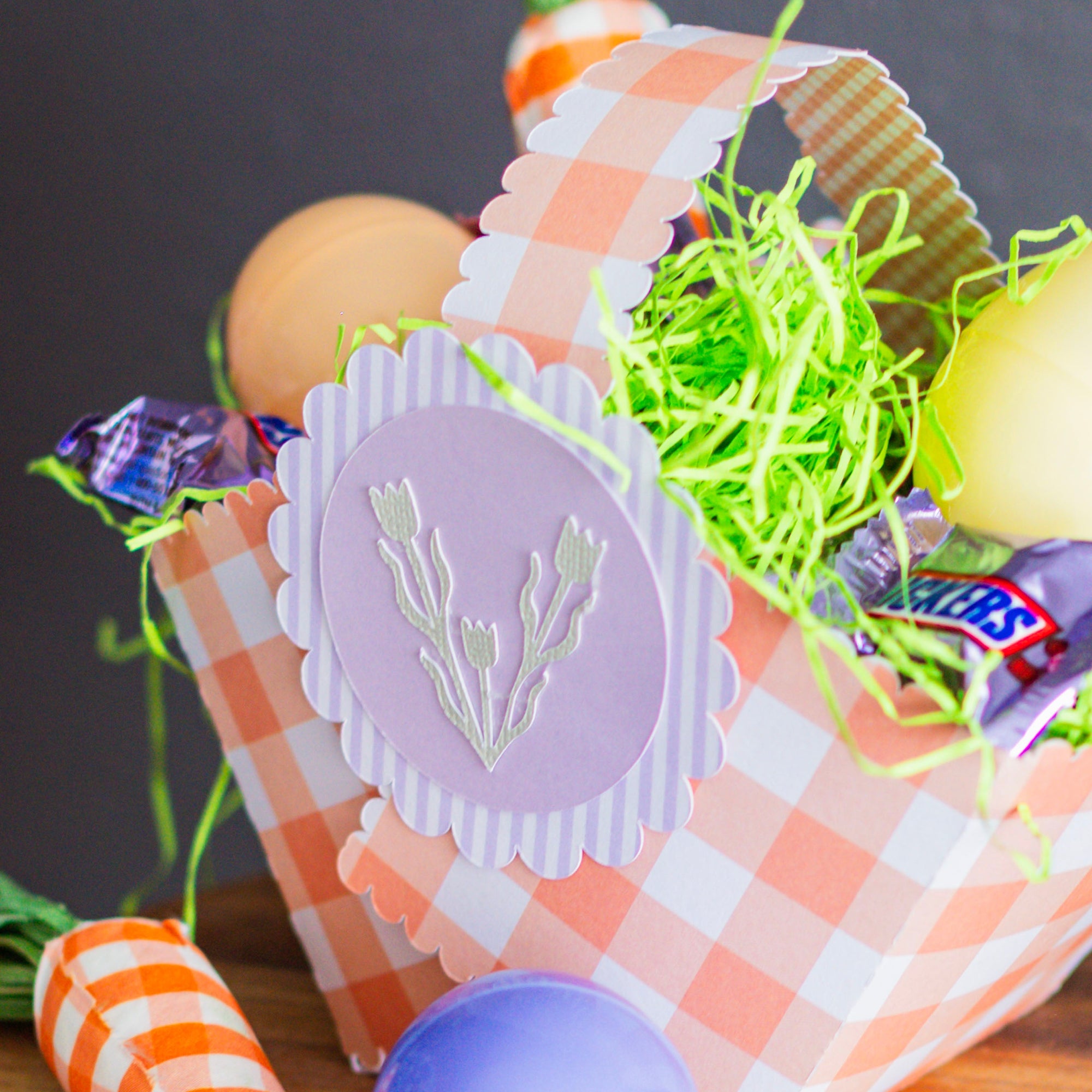 Decorative Easter basket with checkered pattern, candy, and decorative elements on a wooden surface.