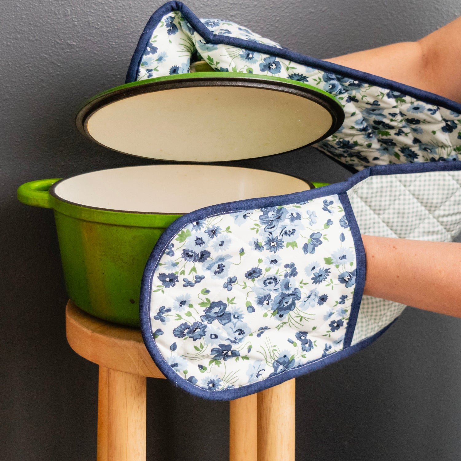 Green pot with floral-patterned oven mitts on a gray background