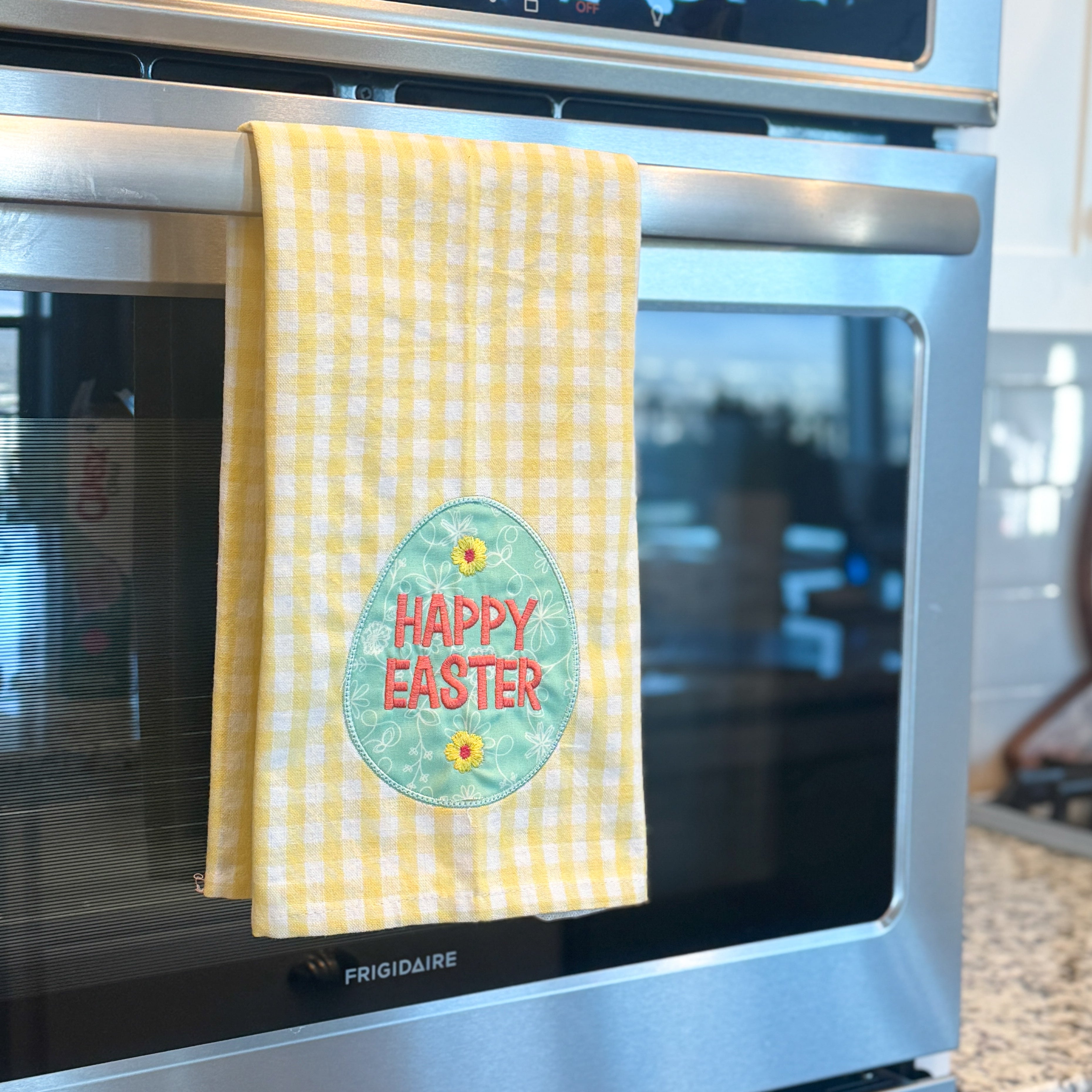 Stainless steel oven with a yellow checkered towel featuring an Easter egg design hanging on the handle.