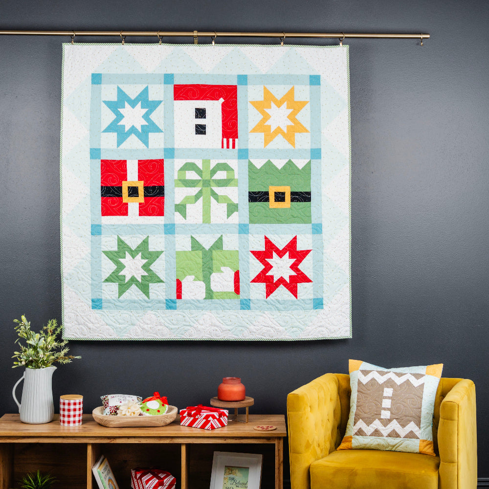 Colorful quilt with geometric patterns hanging on a dark wall above a yellow armchair.