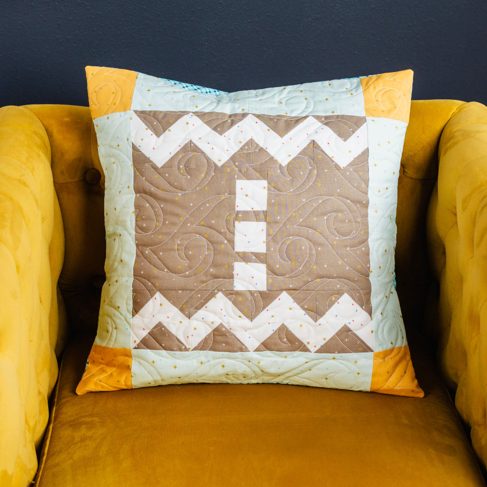 Quilted pillow with geometric pattern on a mustard yellow armchair against a dark background