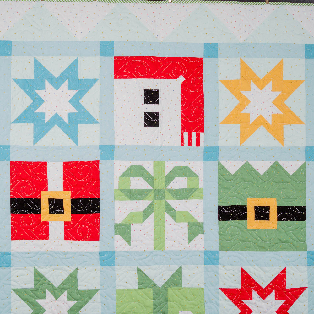 Quilt block with star, house, and bow designs in red, green, blue, and yellow on a light background.
