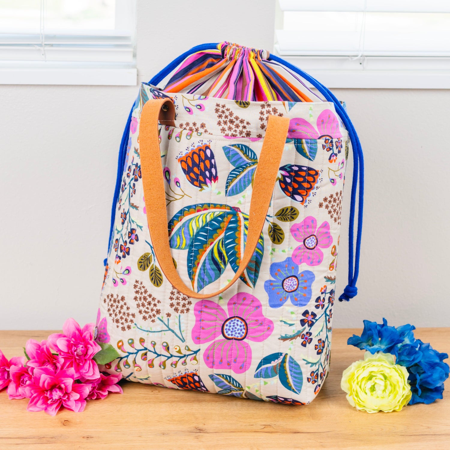 Floral-patterned drawstring bag with a handle on a wooden surface with flowers.
