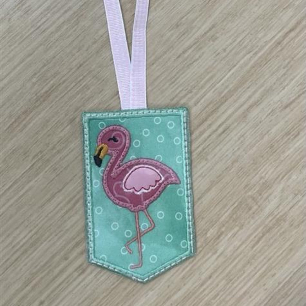 A completed flamingo bag tag with a pink flamingo design on a teal background, with a white ribbon for attaching to bags.