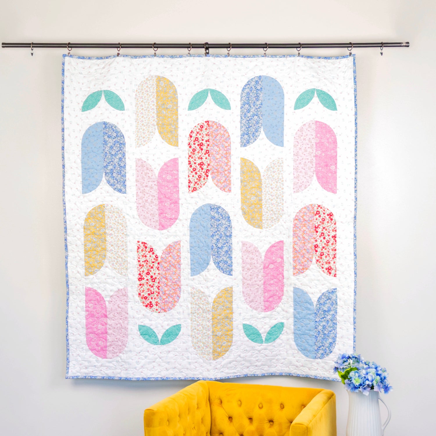 Colorful quilt with abstract pattern hanging on a wall next to a yellow chair.