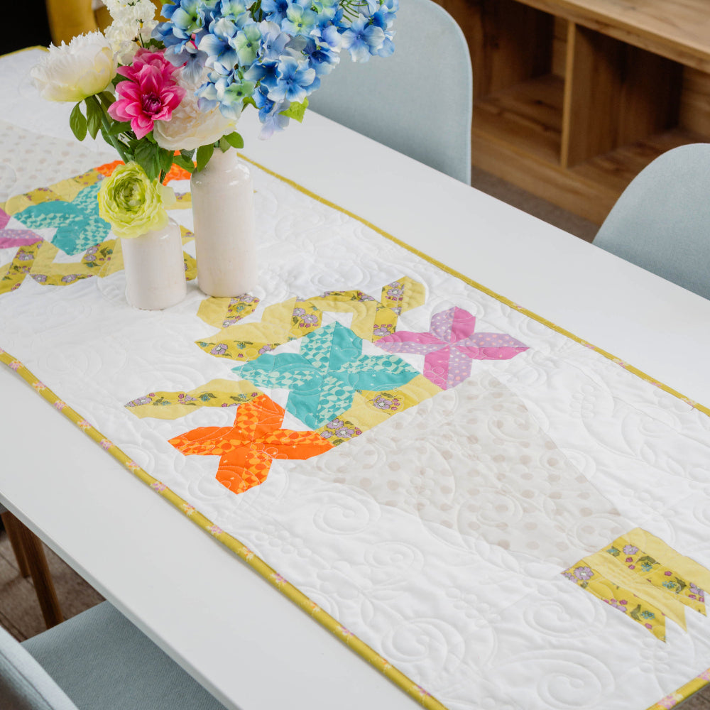 Dining table with a colorful quilted table runner and floral arrangement.