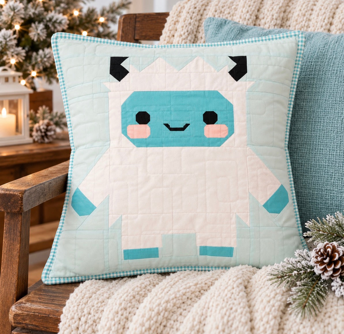 A square quilted throw pillow featuring a cute, pixel-art style white yeti wearing a light blue winter coat, styled on a wooden chair with a cream knit blanket and holiday decorations in the background.