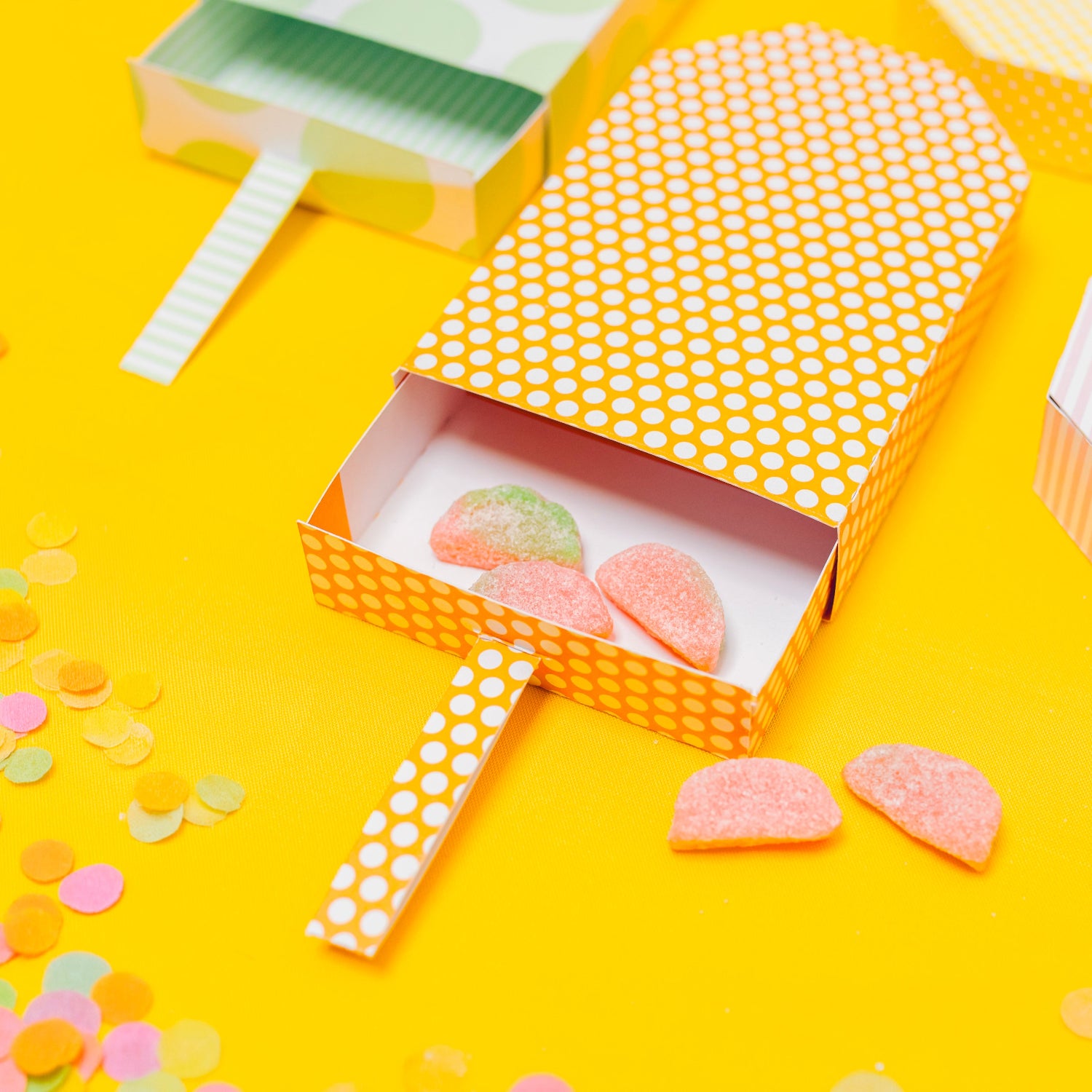 Colorful candy in a hexagonal box on a yellow background with confetti
