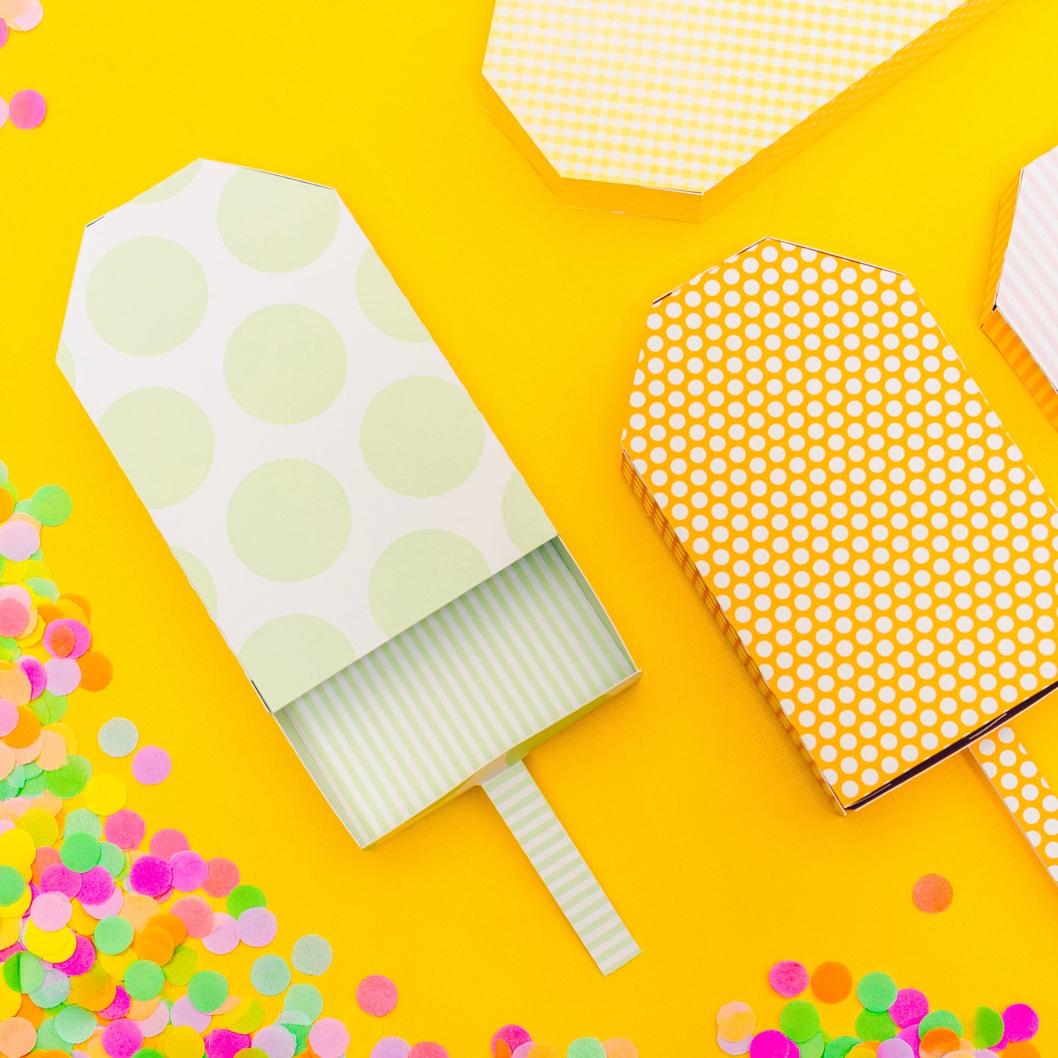 Decorative paper ice cream cones with polka dot patterns on a yellow background with colorful confetti.