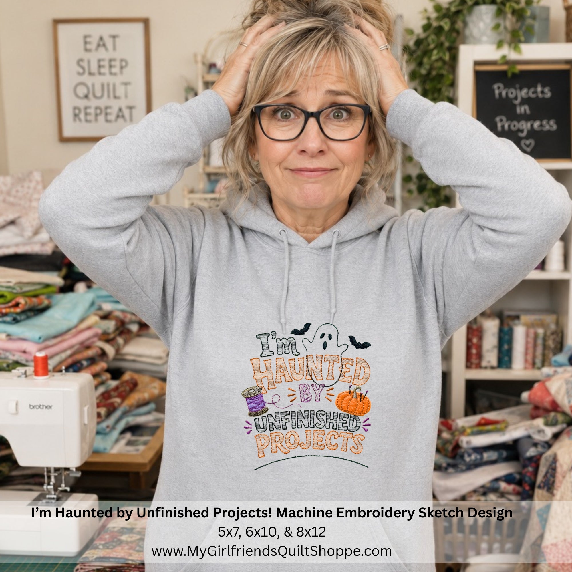 A woman wearing a light gray hoodie with a colorful machine embroidery design that reads 'I'm Haunted by Unfinished Projects' stands in a sewing room. The design includes a ghost, bats, a purple spool of thread, and a small orange pumpkin.