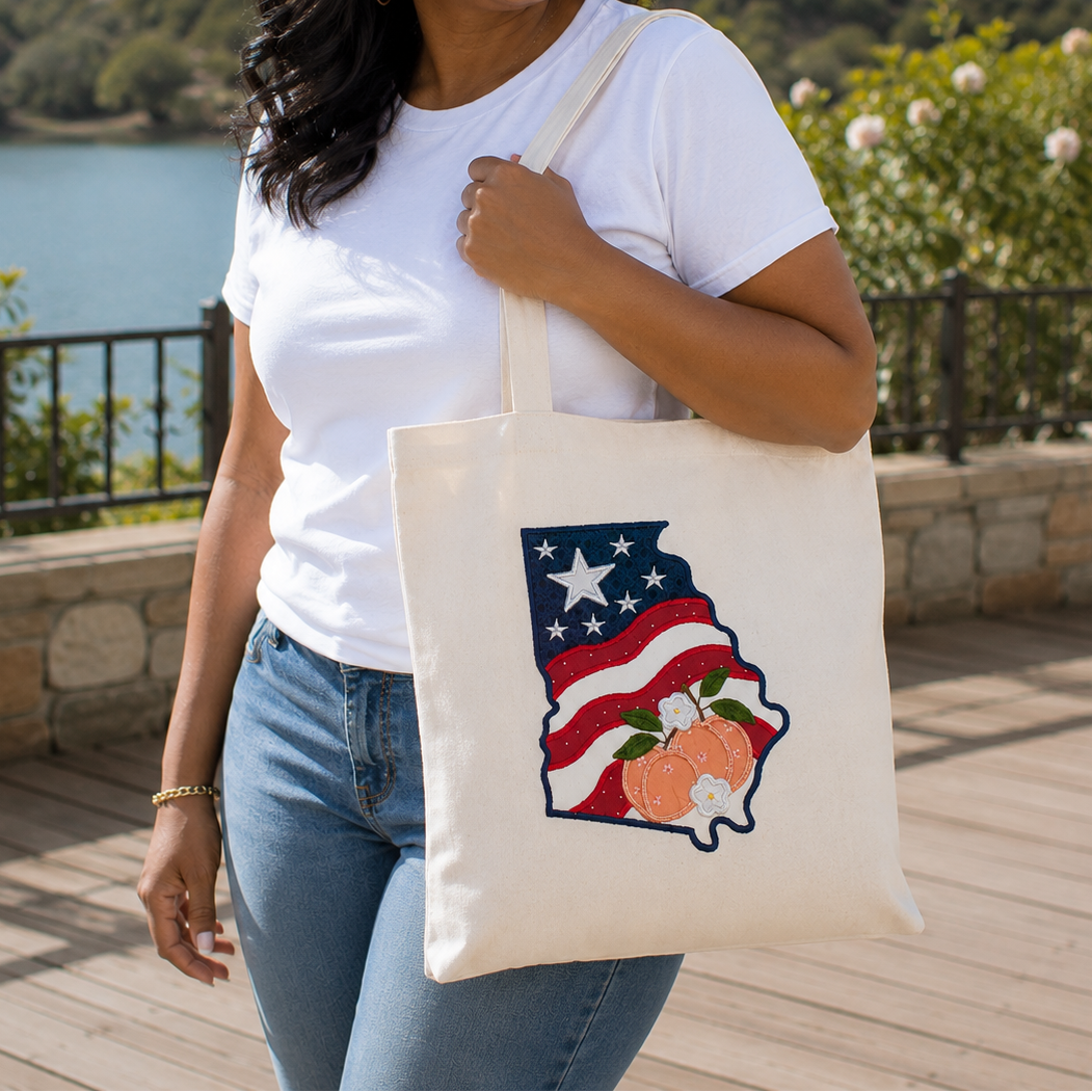 Woman holding a tote bag with a U.S. state design featuring stars and peaches, outdoors.