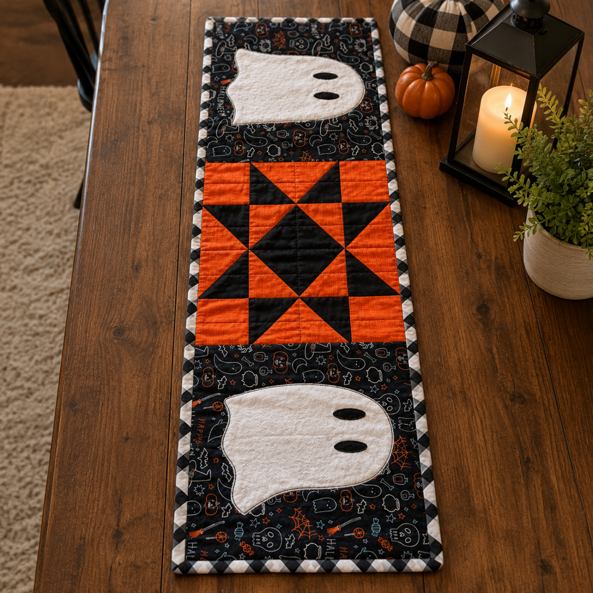 A Halloween-themed quilted table runner displayed on a dark wood dining table. The runner features two white ghost appliqués on a black patterned background and a central orange and black geometric starburst pattern, bordered by a black and white checkered stripe.