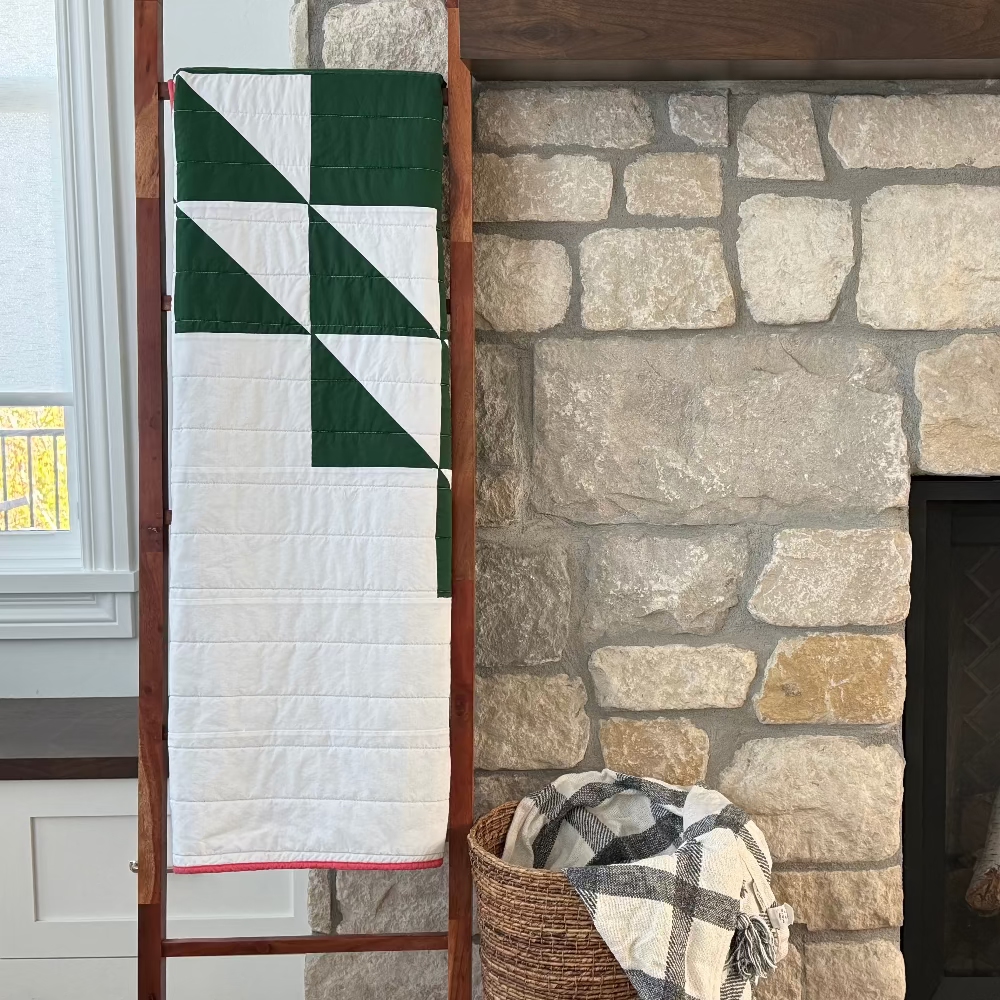 Quilt on a ladder against a stone fireplace with a basket of firewood.