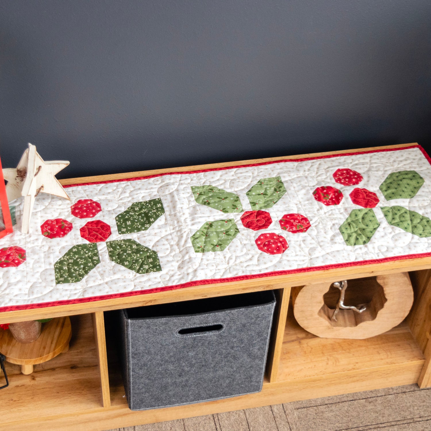 Decorative table runner with red and green patterns on a wooden table against a dark wall.