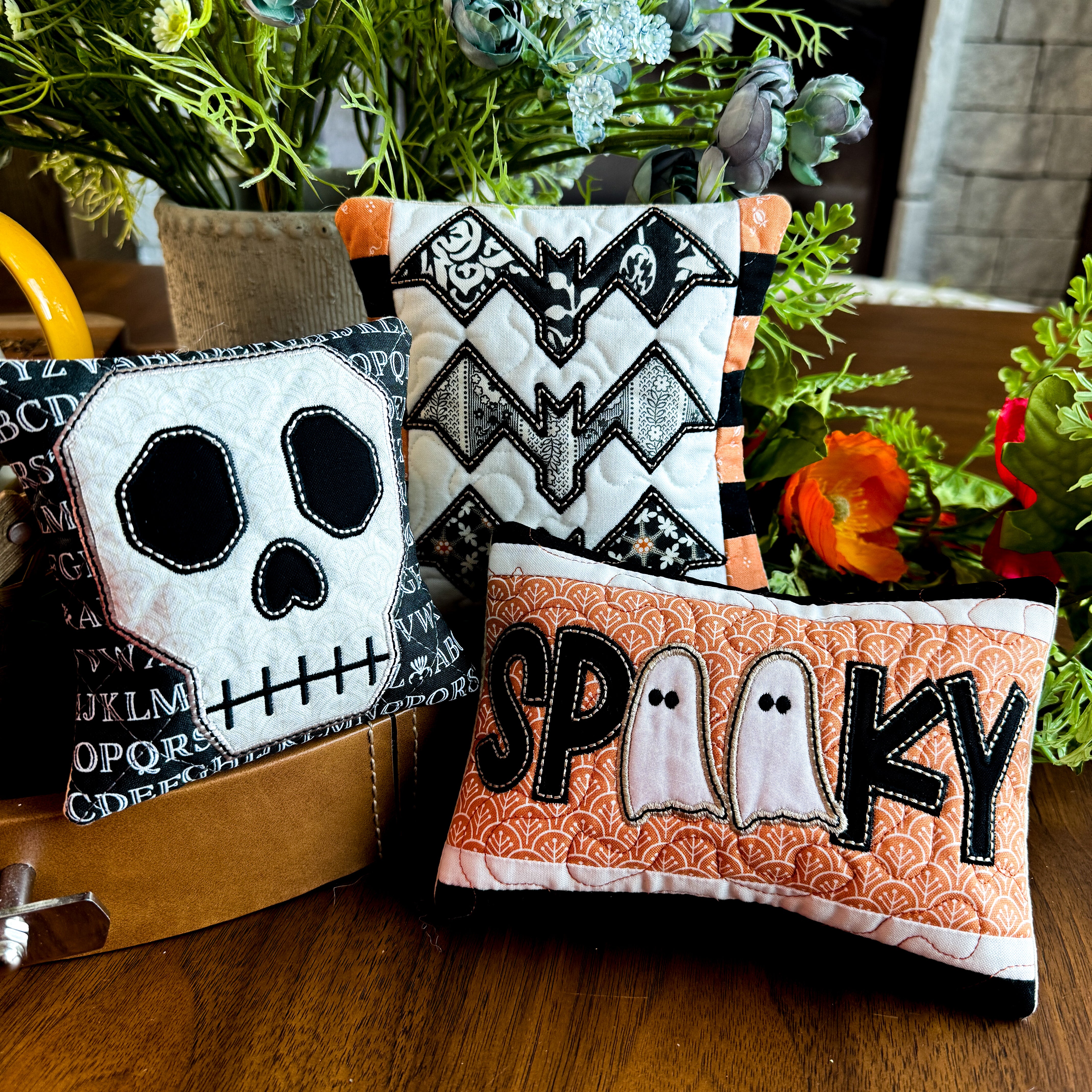 Three Halloween-themed decorative pillows on a wooden surface with plants in the background.