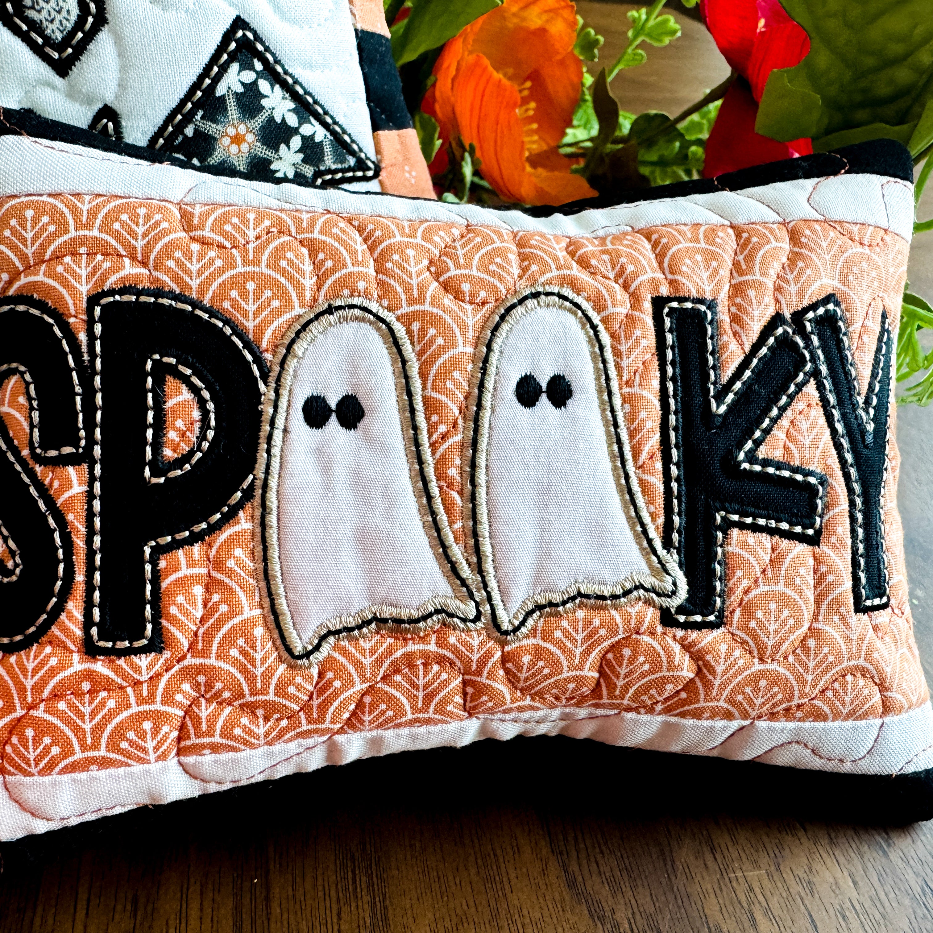 Decorative pillow with 'SPooky' text and ghost designs on an orange patterned background.