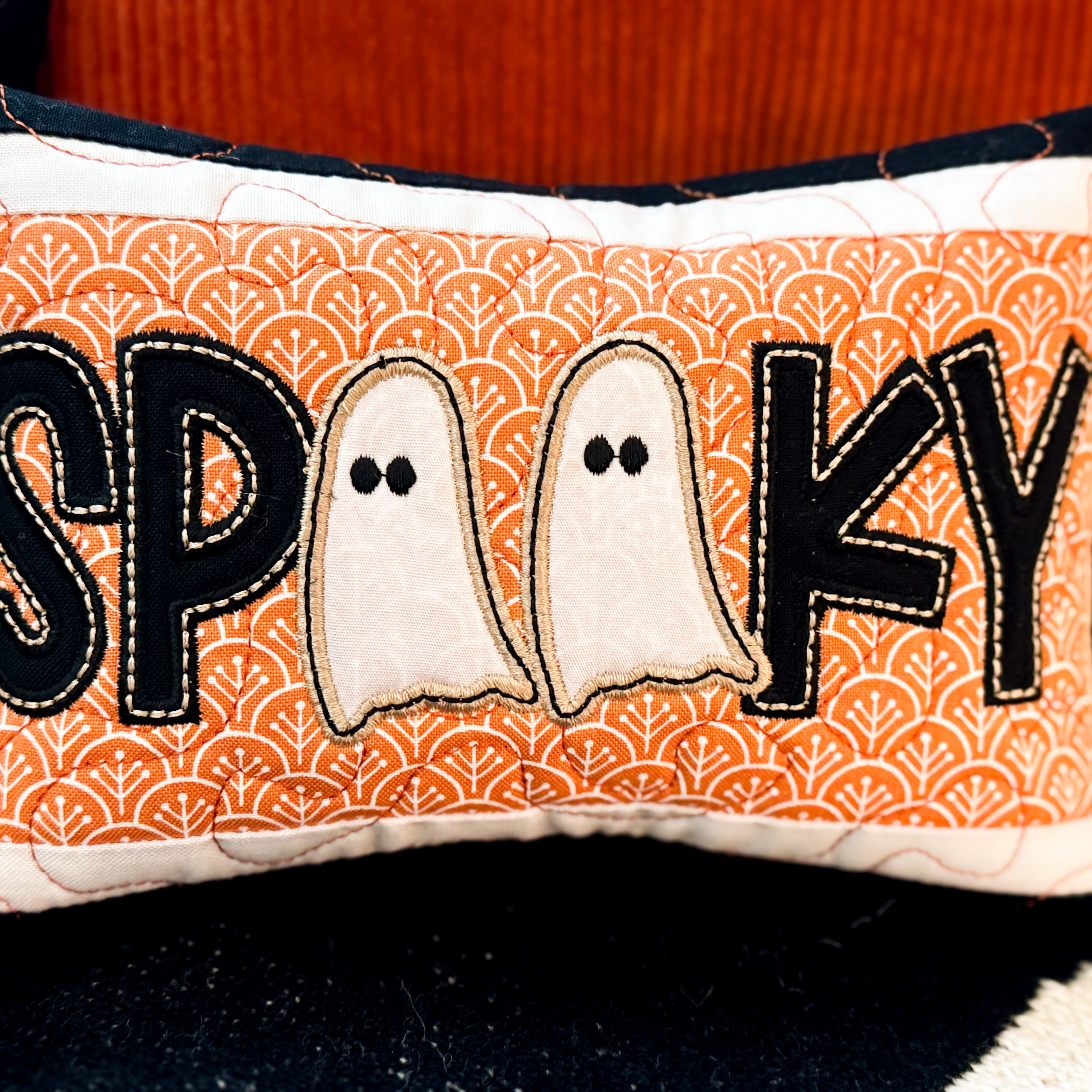 Decorative pillow with 'SPooky' text and ghost designs on an orange patterned background.
