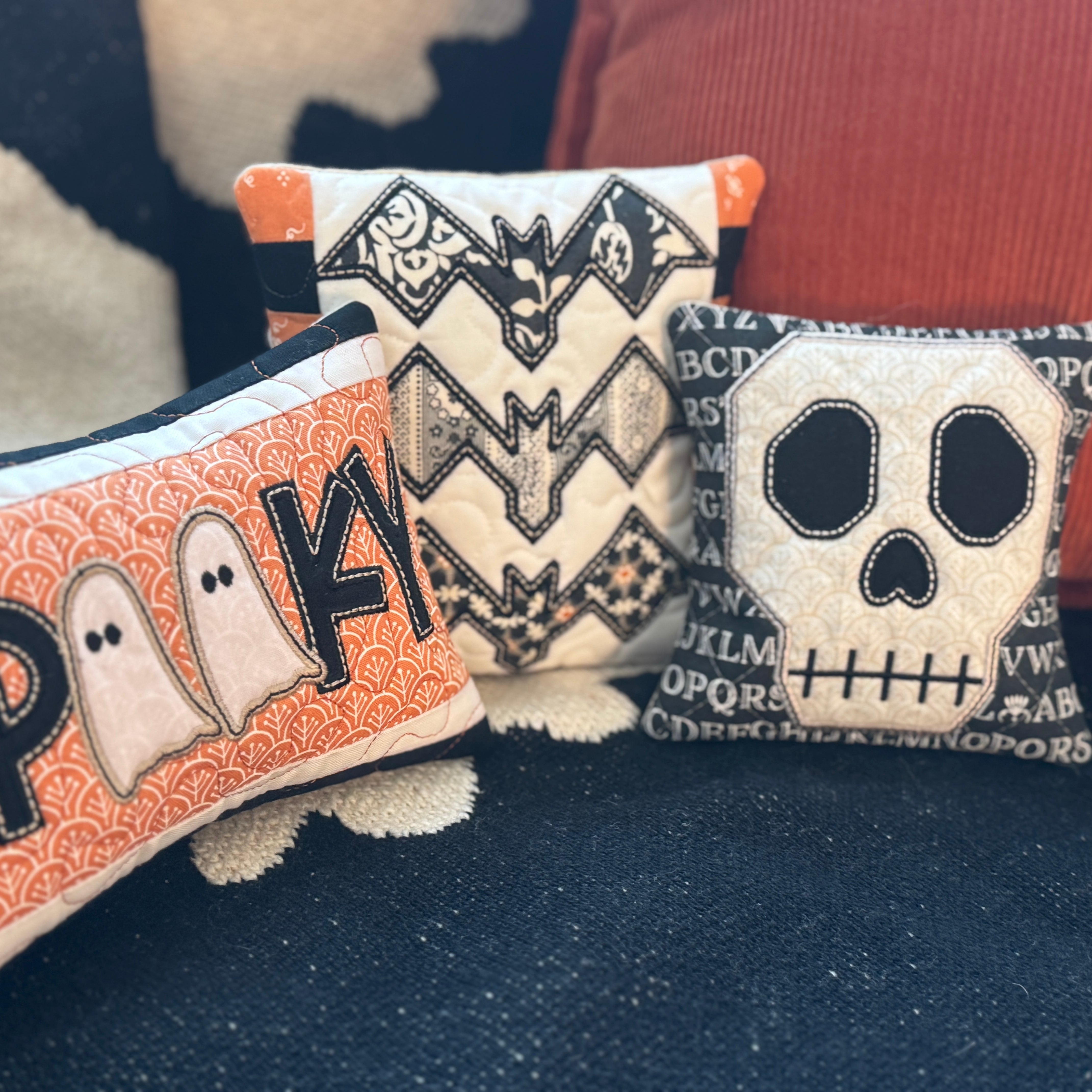 Three Halloween-themed pillows with ghost, bat, and skull designs on a dark surface.