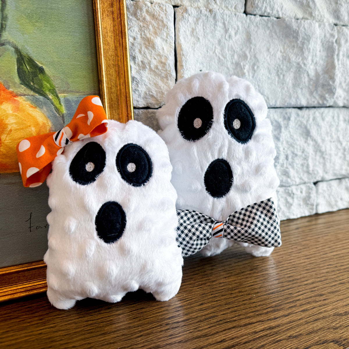 Two plush ghost toys with decorative bows on a wooden surface.