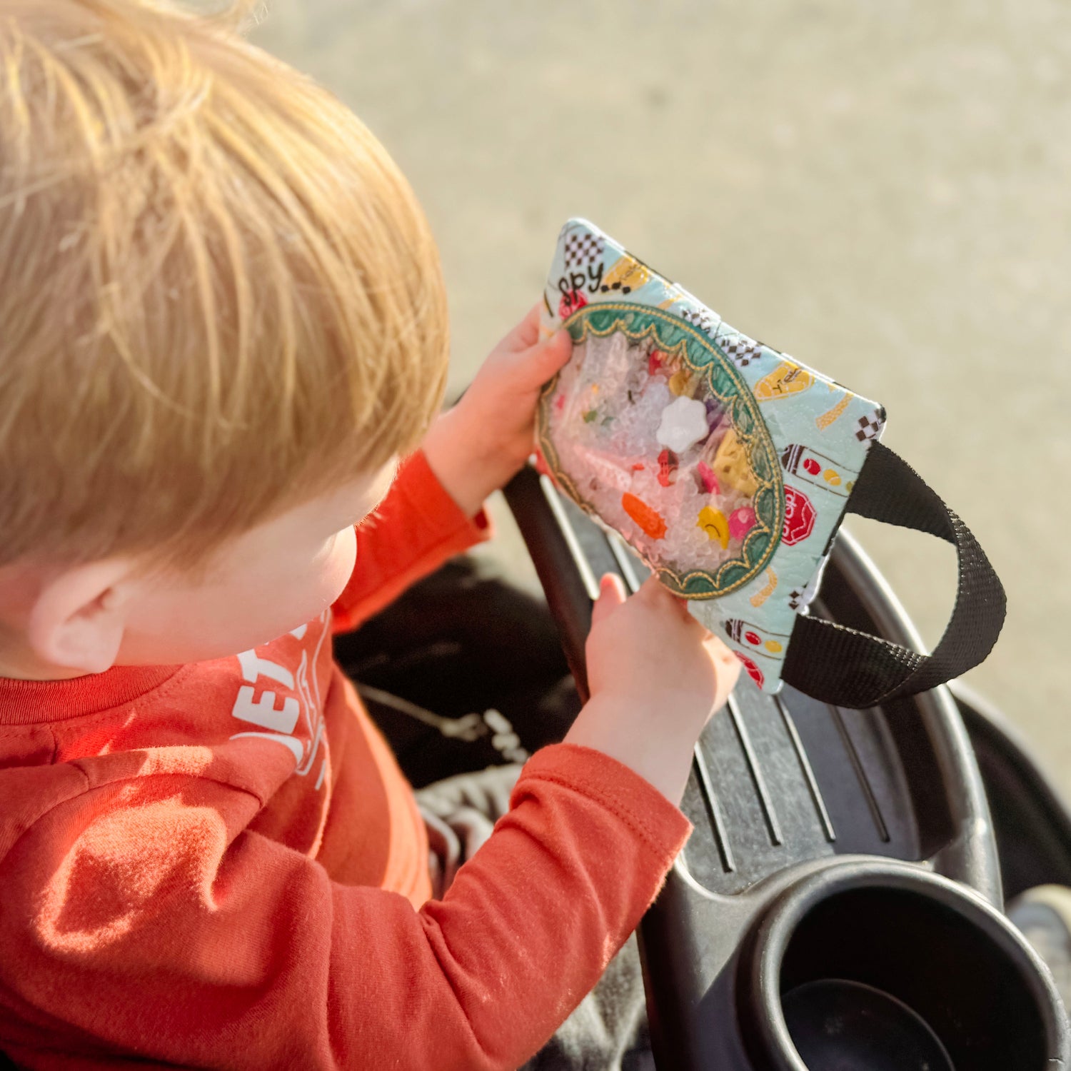 Child in a red shirt holding a colorful book in a car seat.