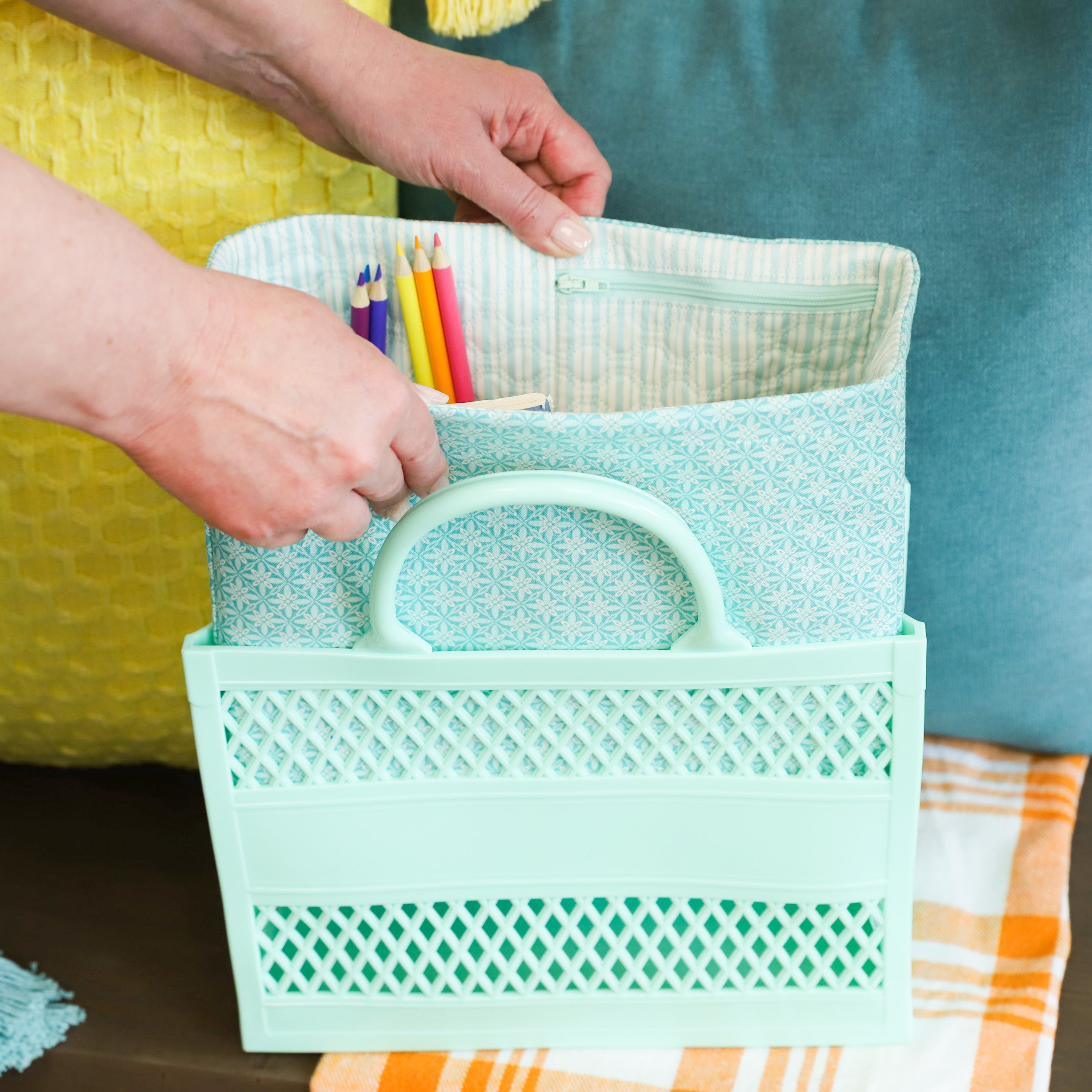Person holding a teal basket with stationery items against a blurred indoor background