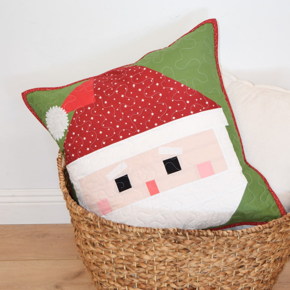 Decorative pillow shaped like a Santa face in a wicker basket on a wooden floor.
