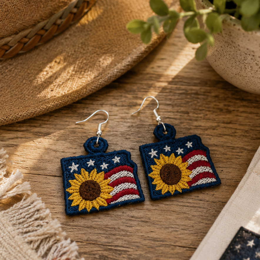 Sunflower-themed earrings on a wooden surface with a hat and plant in the background
