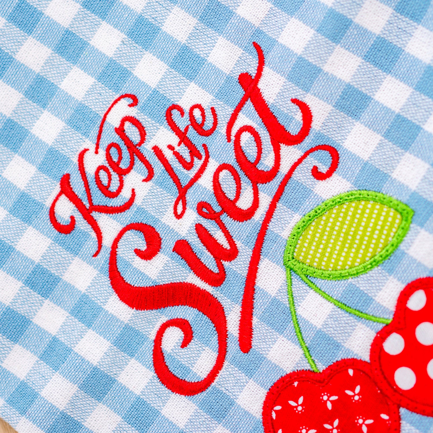 Embroidered text 'Keep Life Sweet' with cherries on a blue and white checkered background