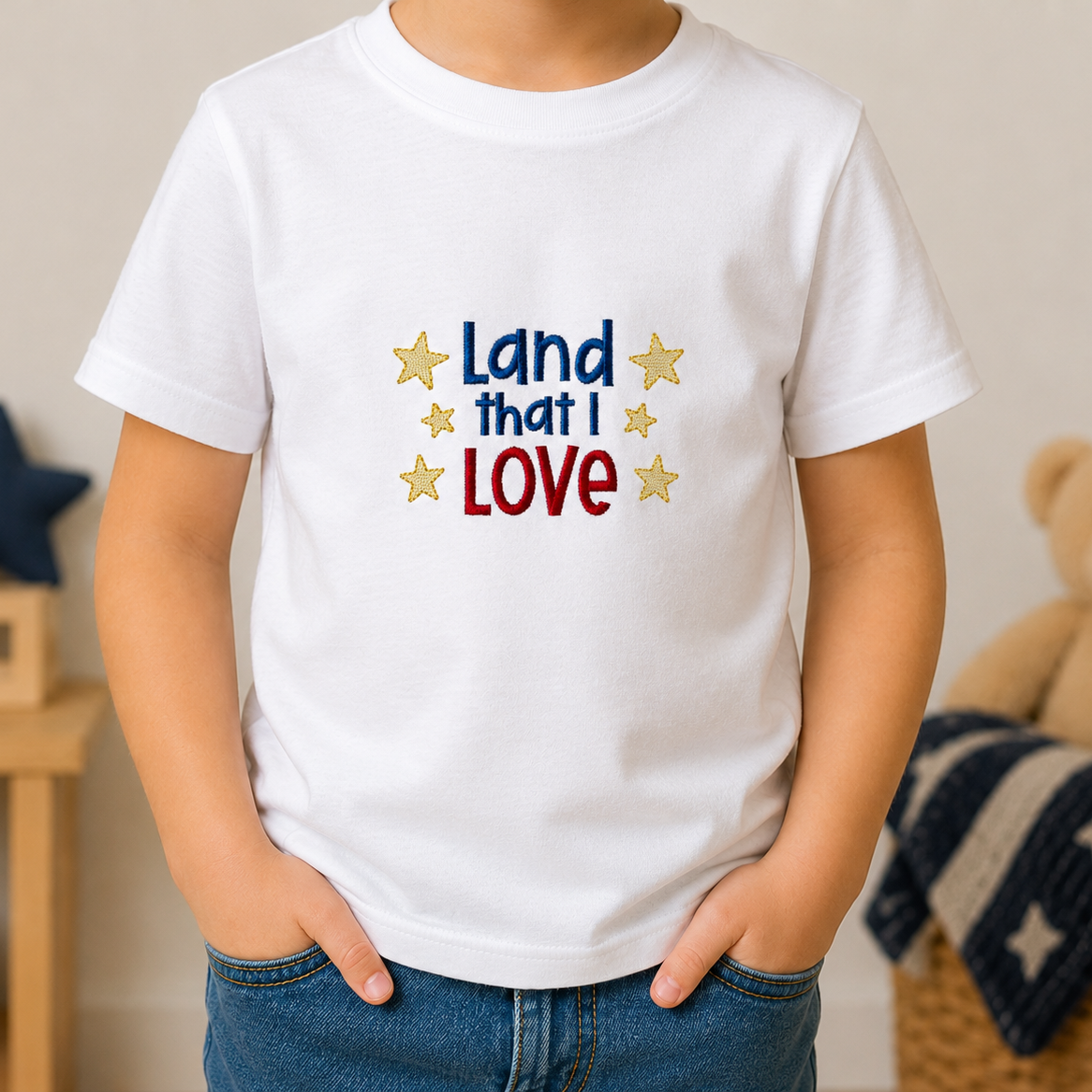 Child wearing a white t-shirt with 'Land that I Love' text and stars, standing in a room with a teddy bear and decorative items.