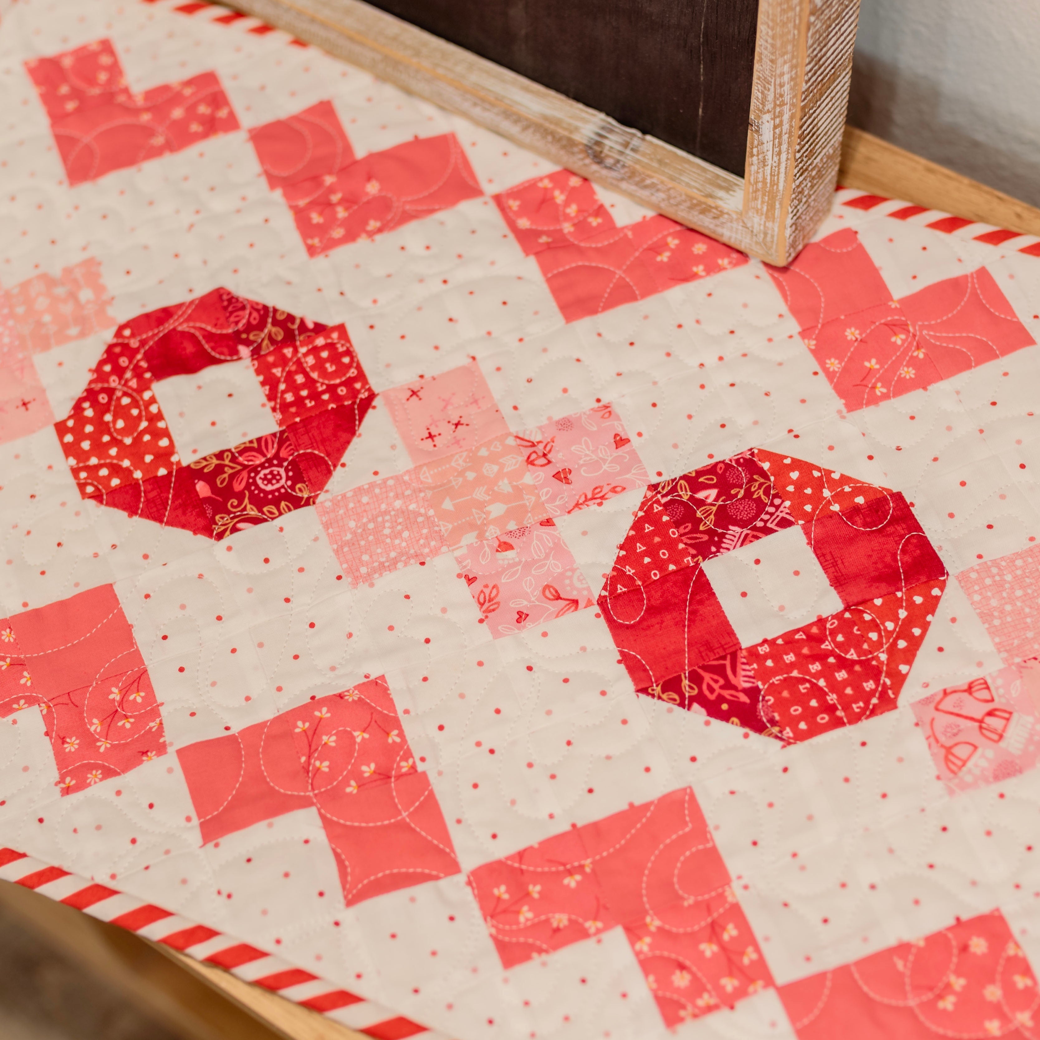 Quilt with red and pink geometric pattern on a wooden surface